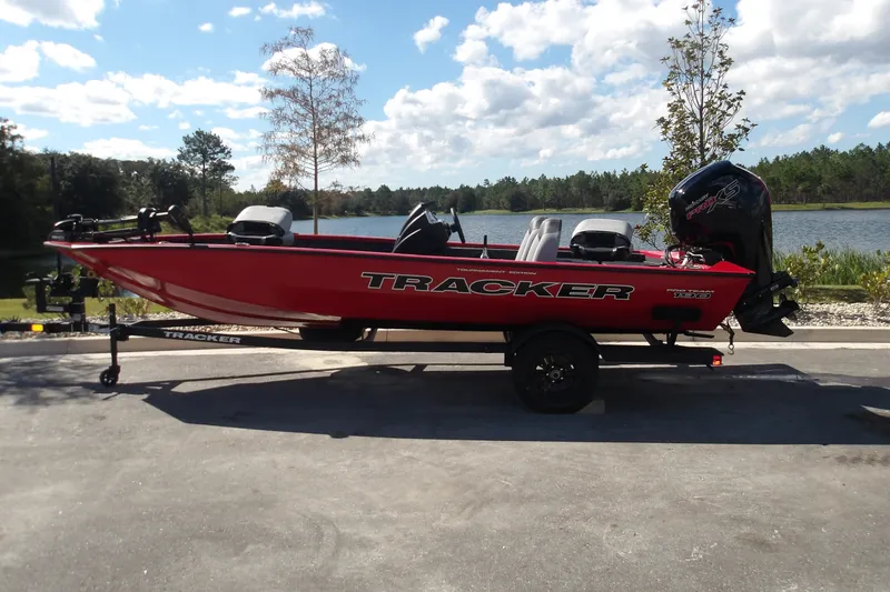 The Image of 2027 Tracker Pro Team 190 boat on trailer by a scenic lake. - 0