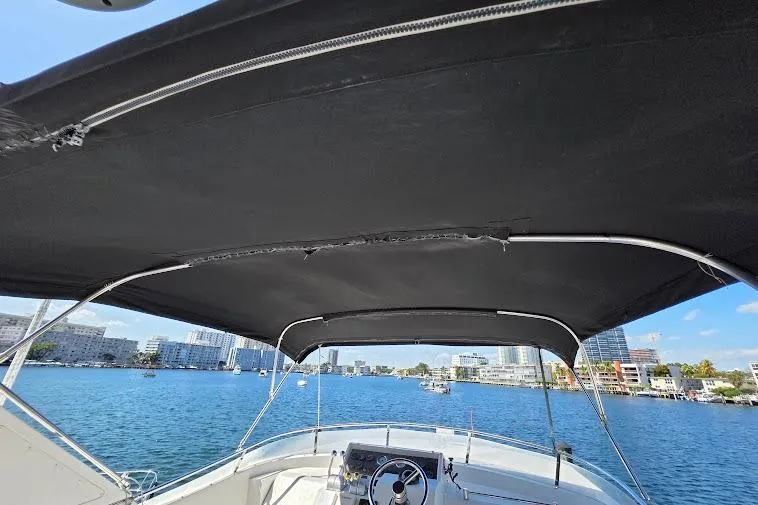 Slide: The Image of 1993 McKinna 48 Pilothouse boat with black canopy, overlooking a scenic waterfront cityscape. - 90