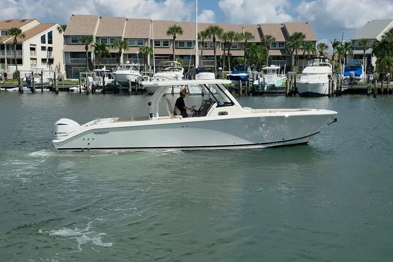 Slide: The Image of 2019 Pursuit S 328 Sport boat cruising in a marina with waterfront homes in the background. - 16