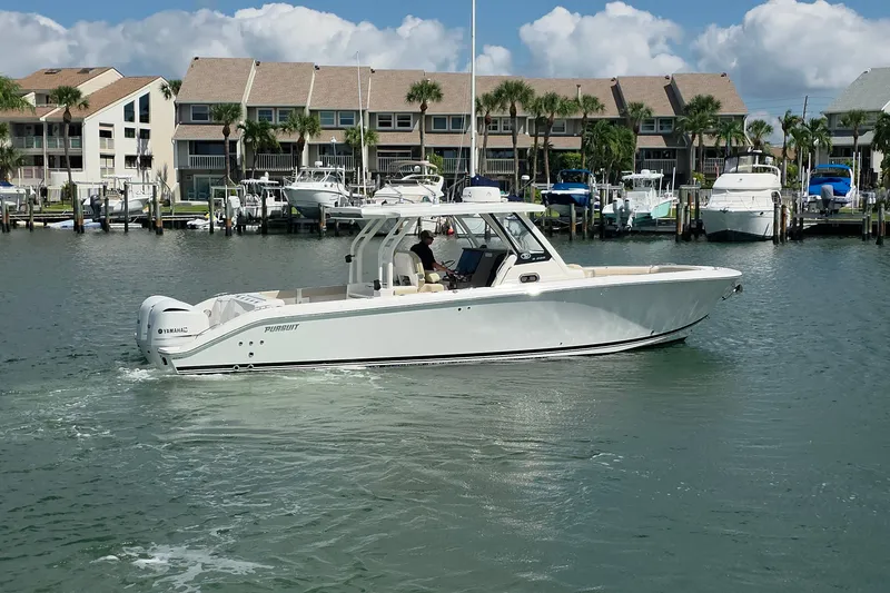 Slide: The Image of 2019 Pursuit S 328 Sport boat cruising in a marina with waterfront homes in the background. - 15