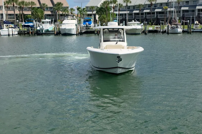 Slide: The Image of 2019 Pursuit S 328 Sport boat cruising in a marina with docked yachts. - 21