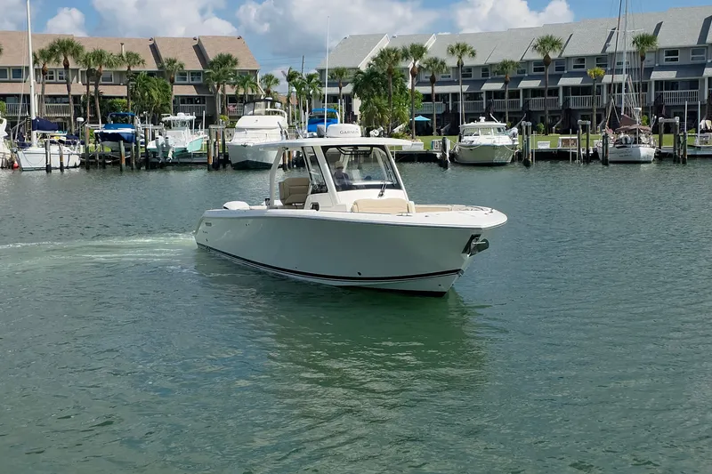 Slide: The Image of 2019 Pursuit S 328 Sport boat cruising in a marina with docked boats. - 20