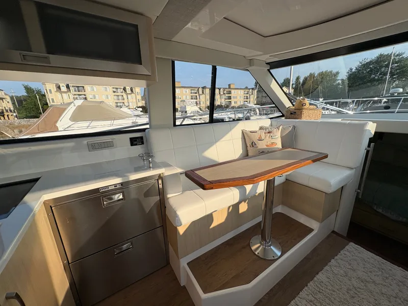 Slide: The Image of Interior of a 2024 Regal 38 Grande Coupe with white seating area and wooden table. - 13