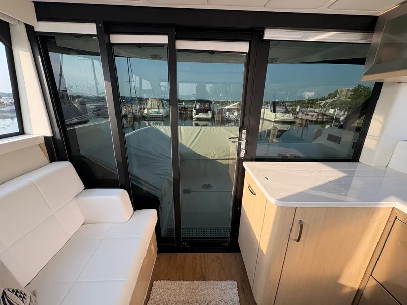 Slide: The Image of Interior of a modern yacht with white leather seating and a kitchenette. Large windows offer harbor views. - 27