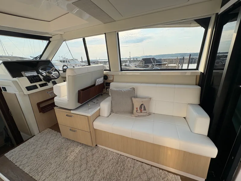 Slide: The Image of Interior of a 2024 Regal 38 Grande Coupe with white sofa and helm station, overlooking the marina. - 14