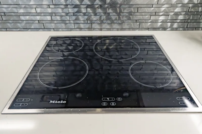 Slide: The Image of Modern Miele induction cooktop with four burners and sleek design, set against a tiled backsplash. - 82
