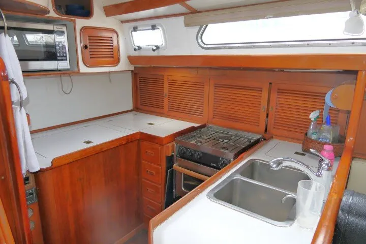 Slide: The Image of 1986 Tayana 52 Center Cockpit yacht kitchen with wooden cabinetry, stove, and dual sink. - 10