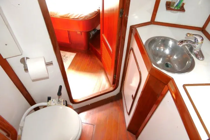 Slide: The Image of 1986 Tayana 52 Center Cockpit bathroom with wooden accents, sink, and toilet. - 46