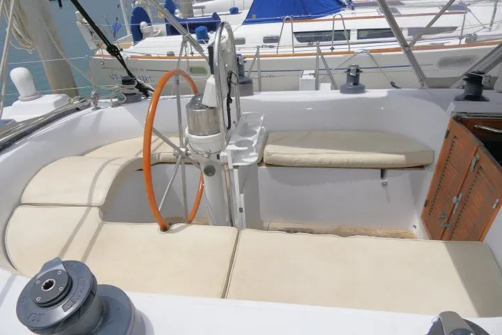 Slide: The Image of 1986 Tayana 52 Center Cockpit with cushioned seating and wooden accents in marina setting. - 52