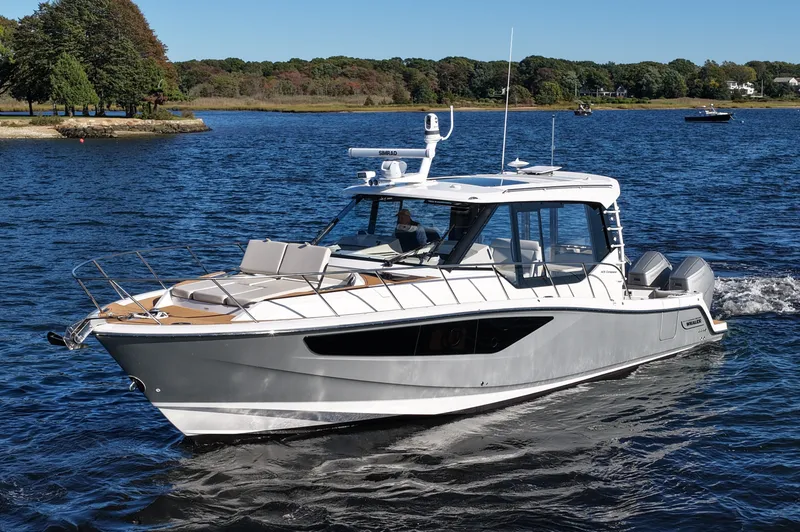 Slide: The Image of The 2024 Boston Whaler 405 Conquest cruises on calm waters with a wooded shoreline in the background. - 14