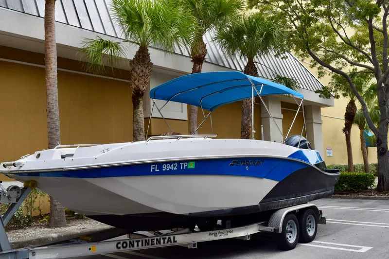 Slide: The Image of 2024 Starcraft SVX 231 OB DH boat on trailer with blue canopy, parked near palm trees. - 2