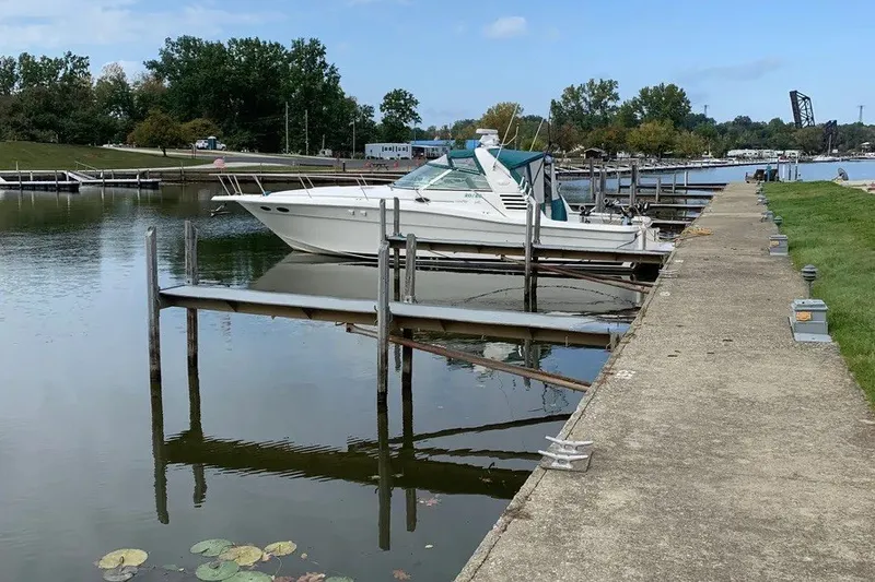 Slide: The Image of 1998 Sea Ray 370 Express Cruiser docked at a serene marina with lush greenery. - 15
