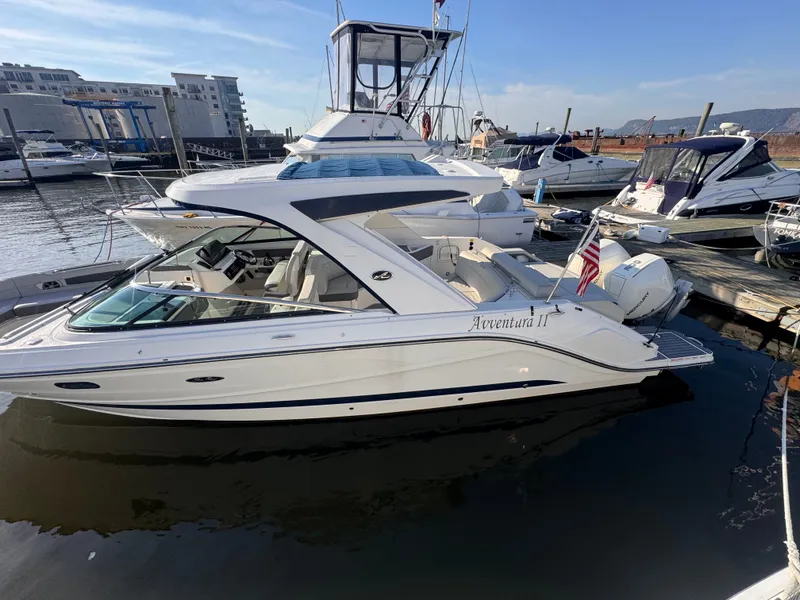 Slide: The Image of 2020 Sea Ray SLX 310 Outboard docked, sleek design, white color, American flag displayed. - 1