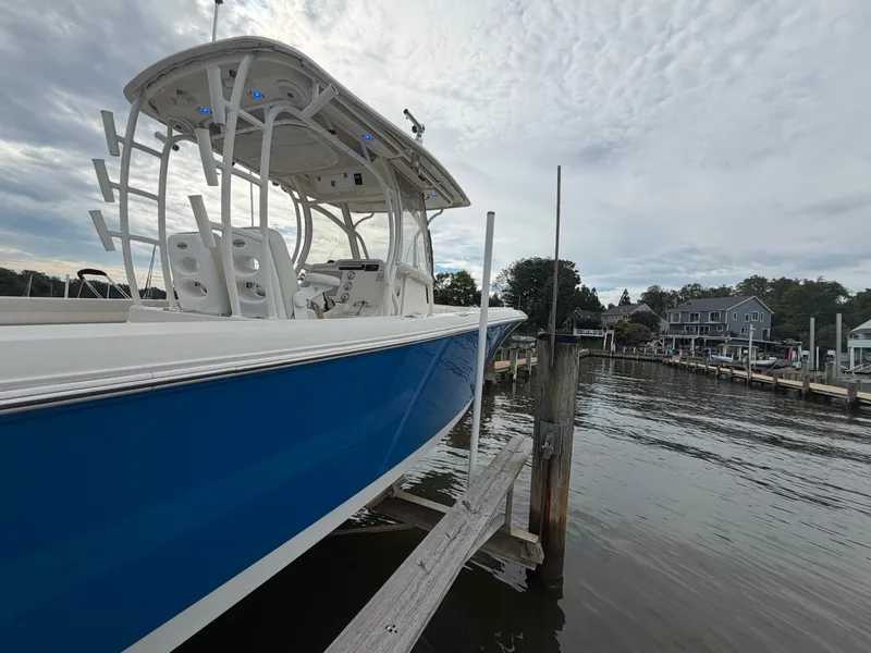 Slide: The Image of A blue and white 2014 Sailfish 290 CC is docked in a calm area under a cloudy sky. - 30