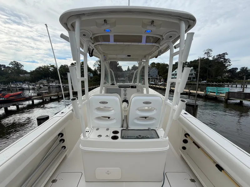 Slide: The Image of The image shows a 2014 Sailfish 290 CC boat at a dock. It features a central console and white seating. - 24