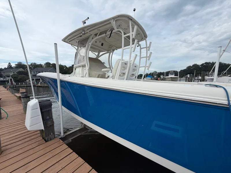 Slide: The Image of A blue 2014 Sailfish 290 CC boat docked at a wooden pier. It features a covered helm. - 7