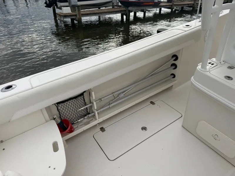 Slide: The Image of The image shows the deck of a 2014 Sailfish 290 CC boat with storage and fishing rod holders. - 26