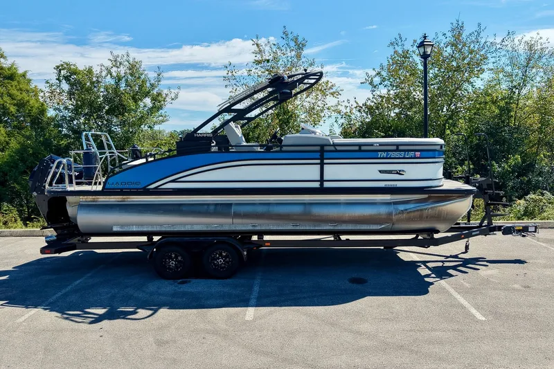 Slide: The Image of 2025 Harris Solstice 230 pontoon boat on trailer, parked outdoors under clear blue sky. - 1