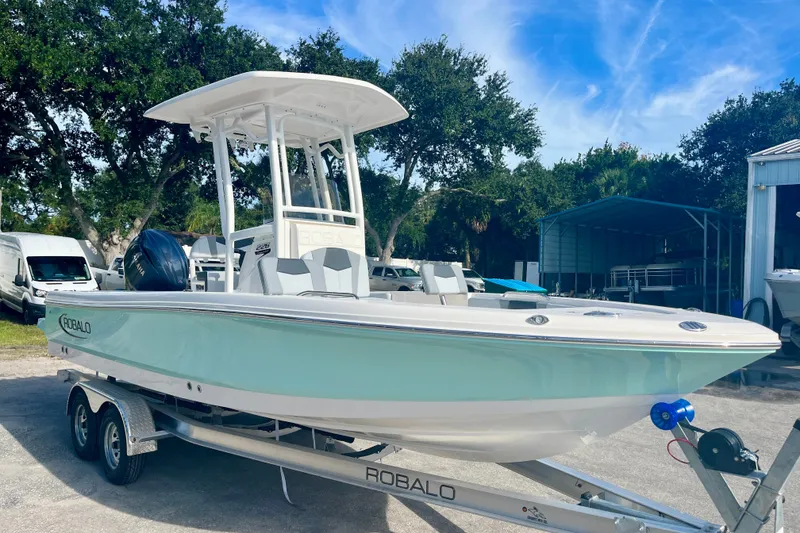 The Image of 2027 Robalo 226 Cayman boat on trailer, parked outdoors under blue sky. - 0
