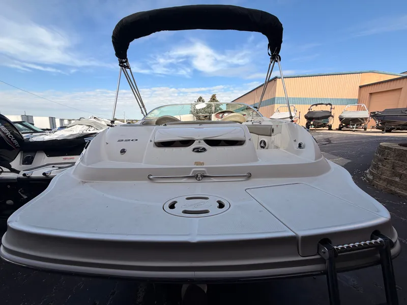 Slide: The Image of A 2006 Sea Ray 220 Sundeck with open deck and Bimini top, parked in a lot. - 7