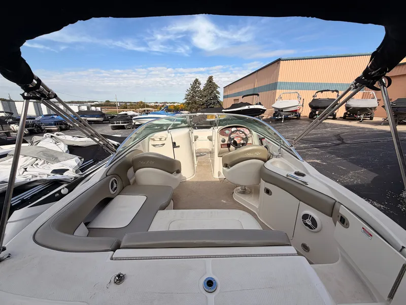 Slide: The Image of The image shows the cockpit of a 2006 Sea Ray 220 Sundeck boat. It features beige and gray upholstery and is parked in a storage area. - 8