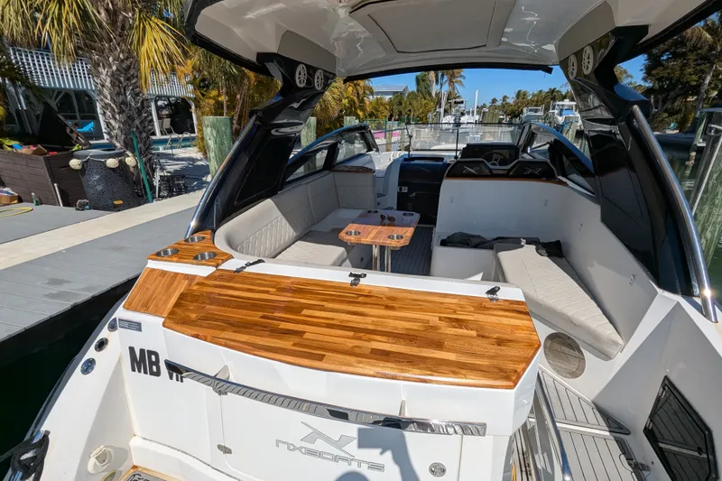 Slide: The Image of 2023 NX Boats 340 Sport Coupe with sleek interior and wooden accents docked by palm trees. - 41