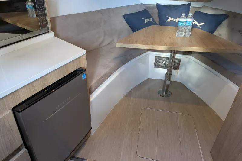 Slide: The Image of Interior of 2023 NX Boats 340 Sport Coupe with seating, table, and mini fridge. - 30