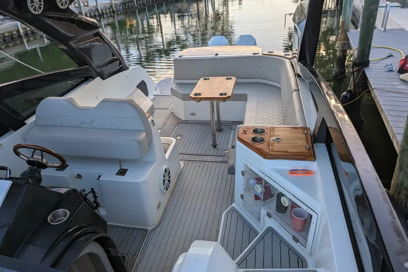 Slide: The Image of 2023 NX Boats 340 Sport Coupe interior with seating, table, and helm at dock. - 19
