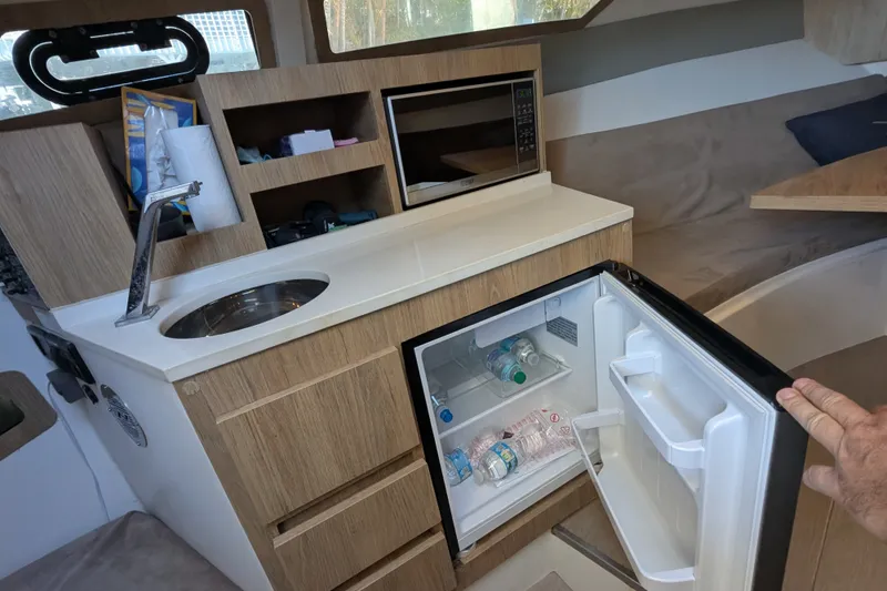 Slide: The Image of Compact kitchen area in 2023 NX Boats 340 Sport Coupe with sink, fridge, and microwave. - 27