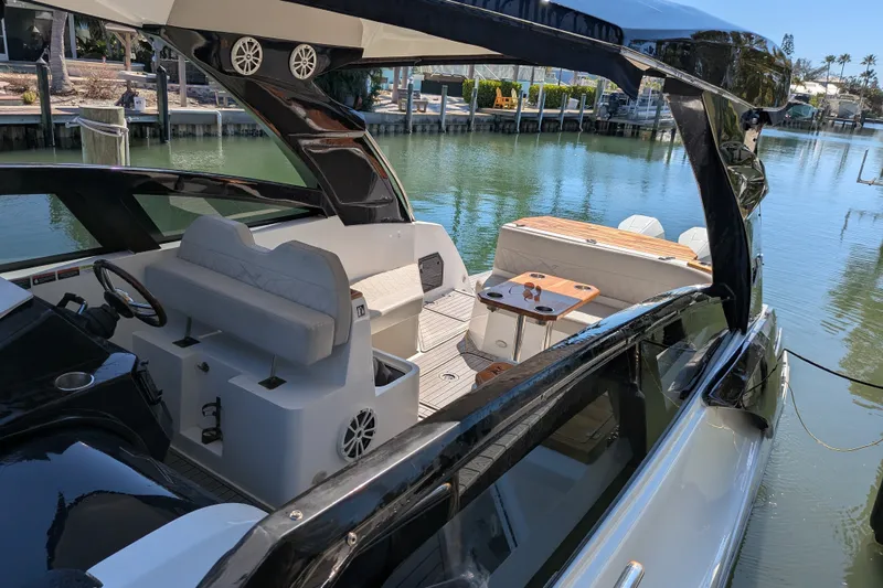 Slide: The Image of 2023 NX Boats 340 Sport Coupe interior with seating and table, docked by the water. - 18