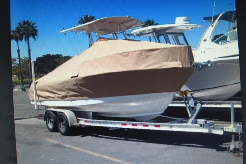 Slide: The Image of 2016 Edgewater 208CC boat covered on trailer, parked outdoors under clear blue sky. - 10