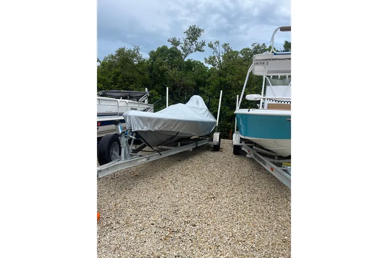 Slide: The Image of Covered V-Tech 18 Flats boat on trailer, parked between two other boats. - 7