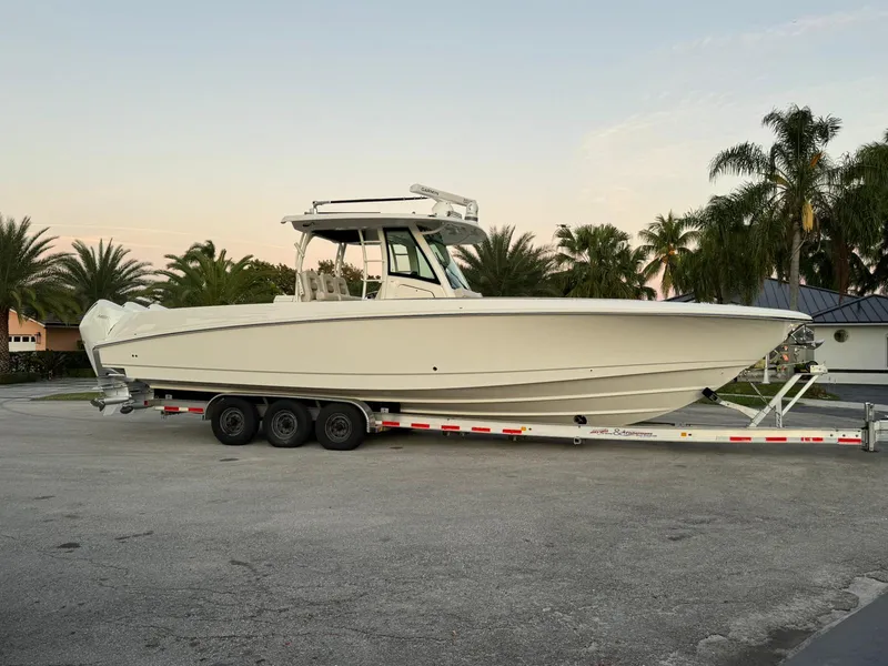 Slide: The Image of 2021 Boston Whaler 350 Outrage boat on a trailer, parked near palm trees. - 2