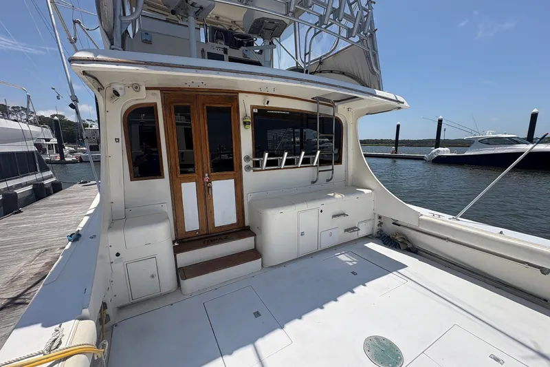 Slide: The Image of 1989 Topaz 44 Sportfisherman boat docked, featuring spacious deck and wooden cabin doors. - 4