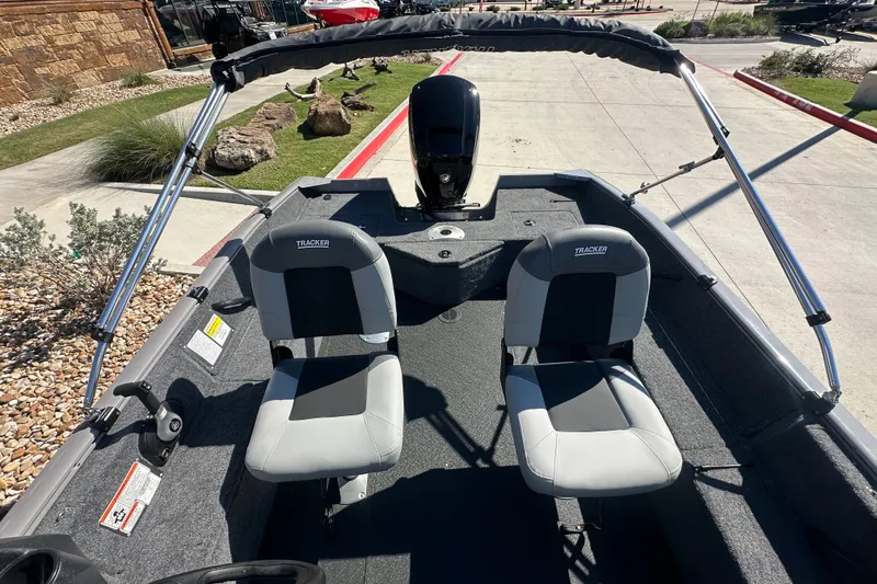 Slide: The Image of 2027 Tracker Pro Guide V-16 WT boat interior with dual seats and motor, parked outdoors. - 23