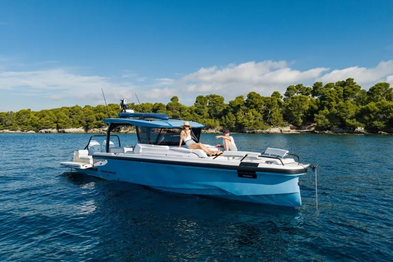 Slide: The Image of 2027 Axopar 38 Cross Top boat cruising on a serene blue sea near a forested shoreline. - 6