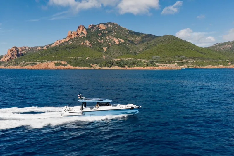 Slide: The Image of 2027 Axopar 38 Cross Top cruising on blue waters near scenic mountainous coastline. - 2