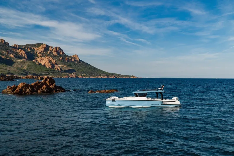 Slide: The Image of 2027 Axopar 38 Cross Top boat cruising near rocky coastline under blue sky. - 9