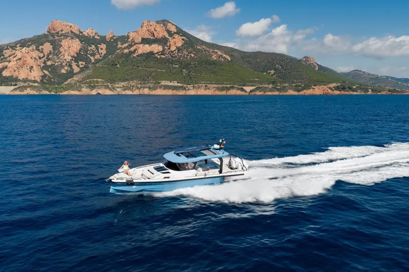 Slide: The Image of 2027 Axopar 38 Cross Top cruising on blue ocean with scenic mountain backdrop. - 4