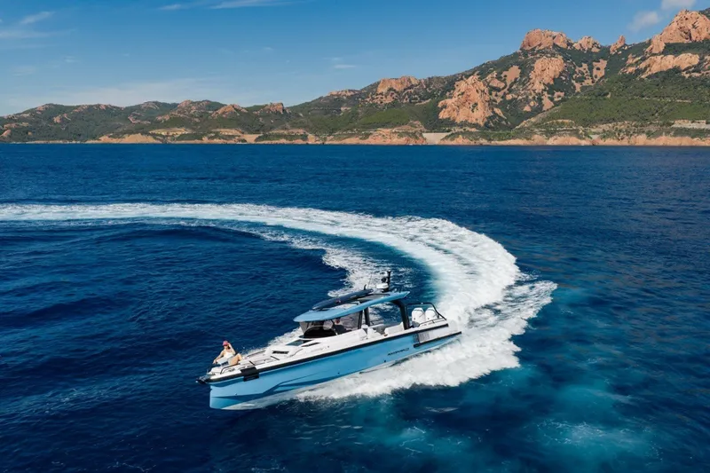 Slide: The Image of 2027 Axopar 38 Cross Top cruising in scenic coastal waters with rocky hills in the background. - 5