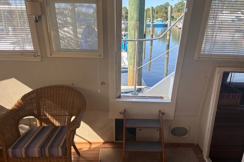 Slide: The Image of Interior view of a 1975 Gulfstar 43 Trawler with wicker chair and marina backdrop. - 67