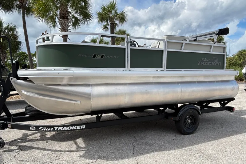 The Image of 2027 Sun Tracker Bass Buggy 16 XL Select pontoon boat on trailer, parked near palm trees. - 0