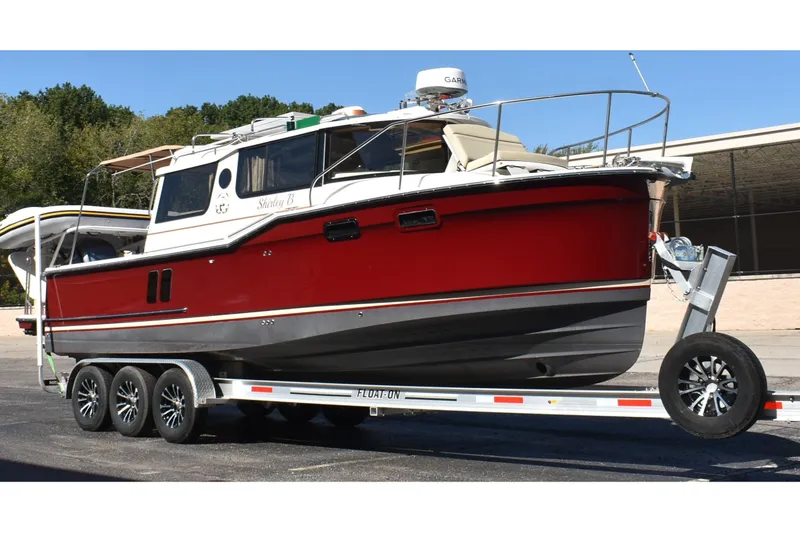 Slide: The Image of 2024 Ranger Tugs R-27 boat on trailer, red hull, parked outdoors. - 1