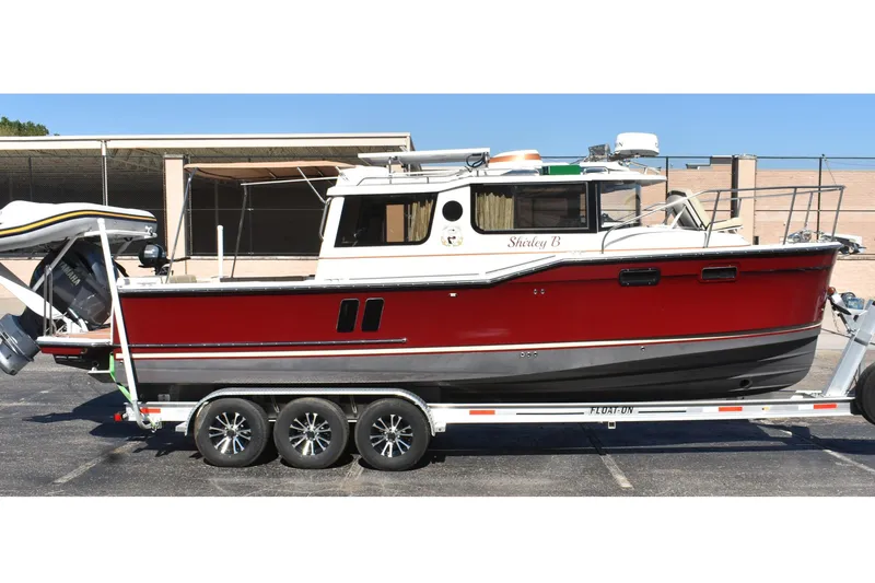 The Image of 2024 Ranger Tugs R-27 boat on trailer, red and white exterior, parked outdoors. - 0