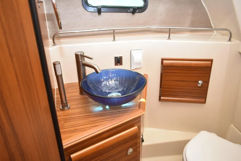 Slide: The Image of 2024 Ranger Tugs R-27 bathroom with blue glass sink and wooden cabinetry. - 43