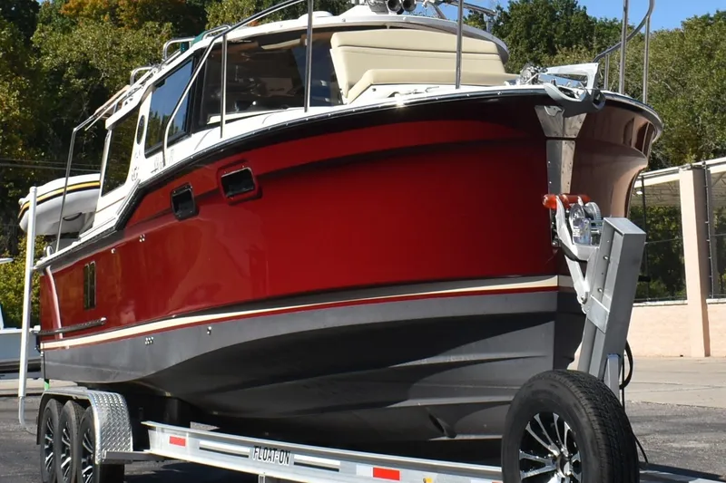 Slide: The Image of 2024 Ranger Tugs R-27 boat on trailer, red hull, parked outdoors. - 6