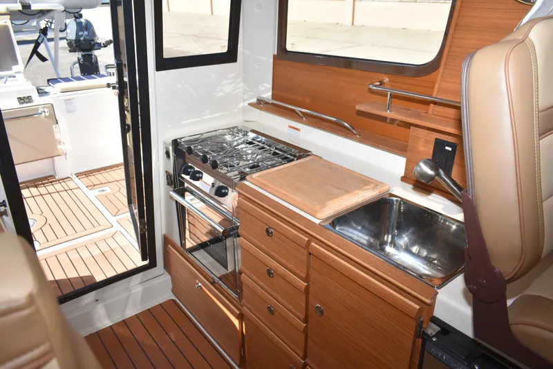 Slide: The Image of 2024 Ranger Tugs R-27 interior kitchen with stove, sink, and wooden cabinetry. - 53