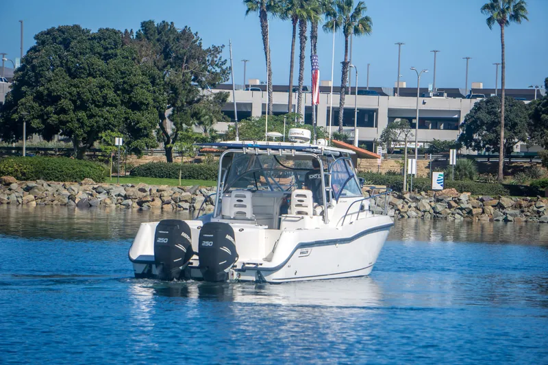 Slide: The Image of 2005 Boston Whaler 305 Conquest boat cruising near a rocky shoreline with palm trees. - 5