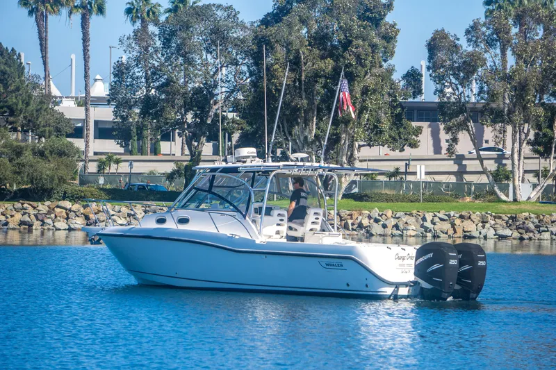 Slide: The Image of 2005 Boston Whaler 305 Conquest boat on calm water near a rocky shoreline. - 6