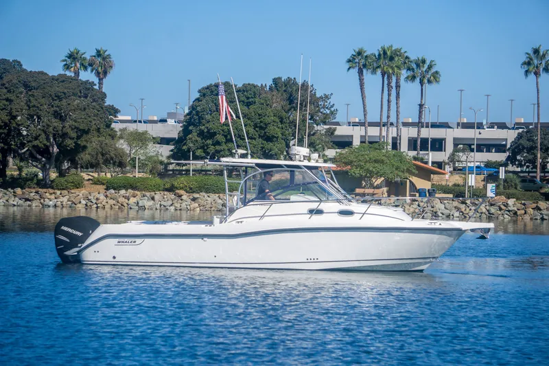 Slide: The Image of 2005 Boston Whaler 305 Conquest boat on calm water, surrounded by trees and buildings. - 1